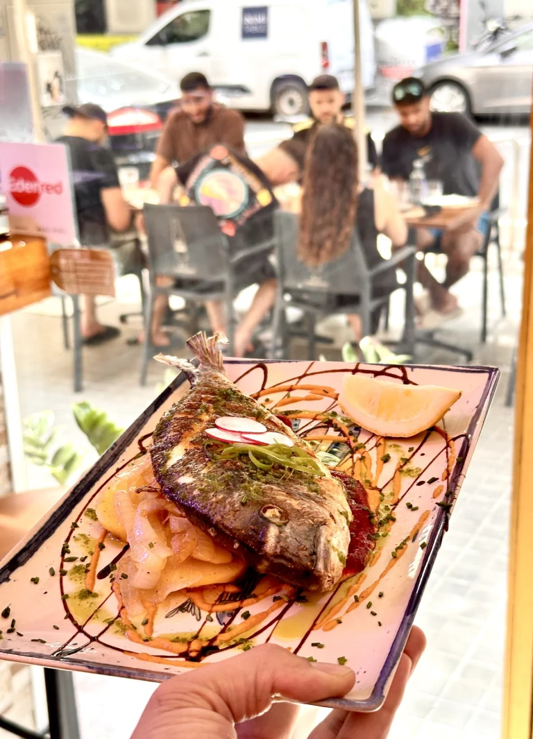 Dorada al horno servida en la terraza de Tastari Mediterrani, con clientes en las mesas de la calle